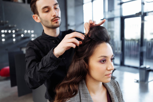 The master does hair styling in a beauty salon. Young woman preparing for a date. - Photo, Image