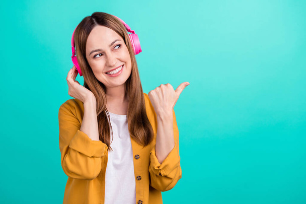 Photo of charming cute mature lady wear yellow shirt enjoying music headphones pointing empty space smiling isolated turquoise color background - Photo, image