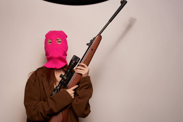 woman in pink mask with a gun in hand Lifestyle beige background - Zdjęcie, obraz
