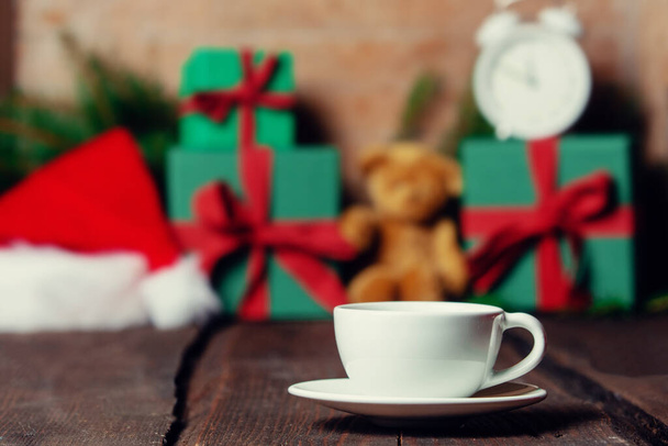 Κύπελλο του καφέ και χριστουγεννιάτικα δώρα στο παρασκήνιο σε ξύλινο τραπέζι. - Φωτογραφία, εικόνα