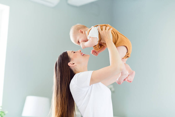 Portrait of attractive careful cheerful gentle affectionate girl playing with baby having fun nursing at light home flat indoors - Foto, Imagen