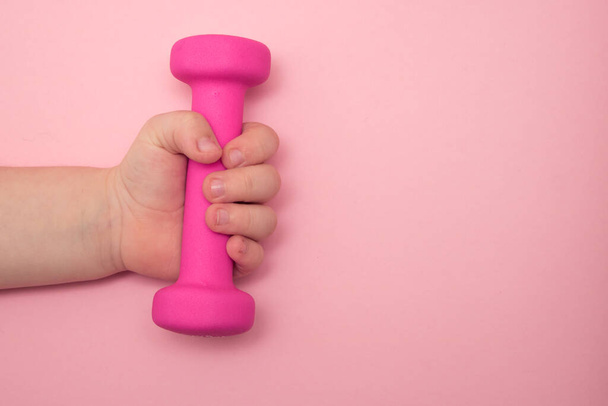 Childrens hand holds a kettlebell on a pink background. Place for text. - Foto, Bild