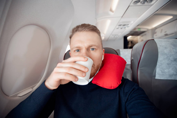 Erkek, uçağın su içen yolcusu, koltukta uyuduğu için yastığı seviyor. Güvenli maskeyle seyahat etmeyi kabul et - Fotoğraf, Görsel