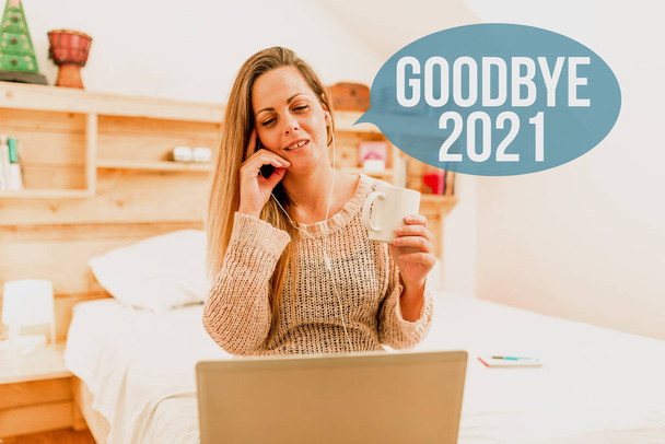 Conceptual display Goodbye 2021. Business concept express good wishes when parting or at the end of last year Woman vediocalling through laptop from bedroom with wired headphones - Photo, Image