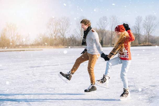 Milující pár v teplých svetrech se baví na ledě. Žena a muž bruslí venku za slunečného sněhového dne. Aktivní rande na ledové aréně v zimě Štědrý den. Romantické aktivity a koncepce životního stylu. - Fotografie, Obrázek