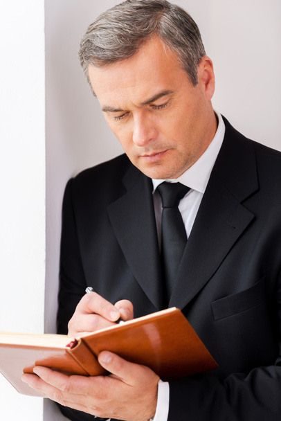Mature man in formalwear writing in note pad - Photo, image