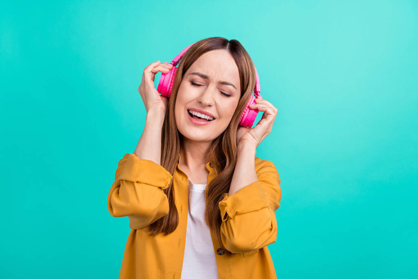 Photo of charming pretty young woman dressed yellow shirt smiling listening songs earphones singing isolated teal color background - Fotografie, Obrázek
