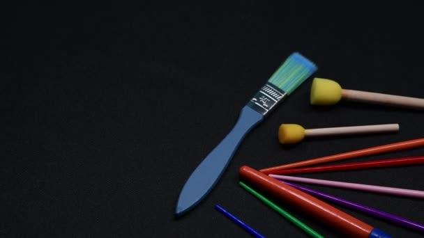 Una selección de pinceles de arte y artesanía para niños y esponjas de diferentes colores desplegadas a través de un fondo oscuro. - Metraje, vídeo