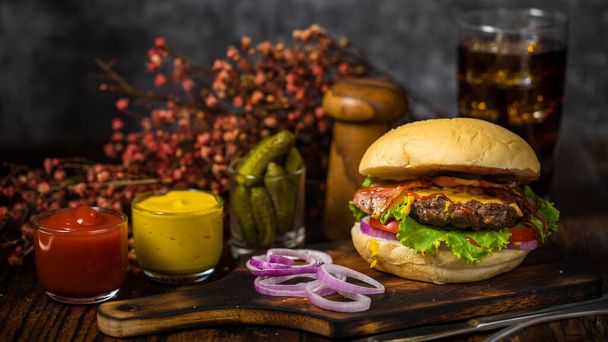 Selektywny nacisk na hamburgery z hamburgerami wołowymi, smażoną cebulą, szpinakiem, ketchupem, pieprzem, sosem musztardowym i serem serwowane świeże cebule na drewnianej desce z napojem bezalkoholowym w tle poddasza - Zdjęcie, obraz