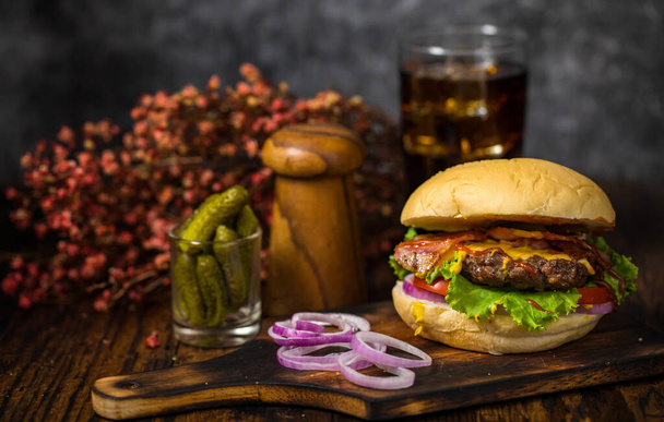 Selektivní zaměření na hamburgery s hovězím masem, smaženou cibulí, špenátem, kečupem, pepřem, hořčičnou omáčkou a sýrem podávané čerstvé cibule na dřevěné desce s nealkoholickým nápojem v podkroví - Fotografie, Obrázek