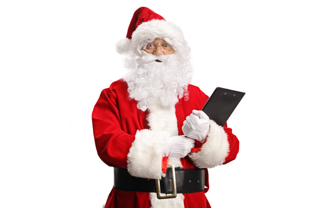 Sorprendido Santa Claus sosteniendo un portapapeles y mirando a la cámara aislada sobre fondo blanco - Foto, Imagen