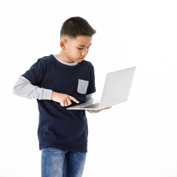 Cutout portrait of smart Asian boy on grey sweater and denim blue shirt wisely standing and concentrate on playing compact laptop he comfortably holding to search for online info of digital technology - Photo, image