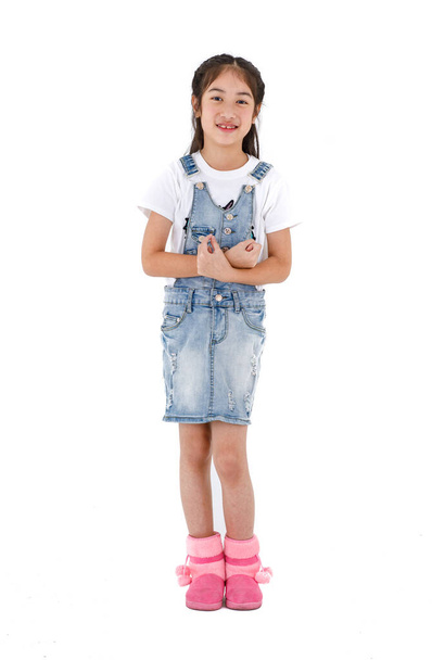 Portret close-up geïsoleerde studio shot van Aziatische kleine schattig meisje draagt T-shirt en coole jeans denim rok overalls staande glimlachende blik op camera gekruiste armen op de borst in de voorkant van witte achtergrond. - Foto, afbeelding