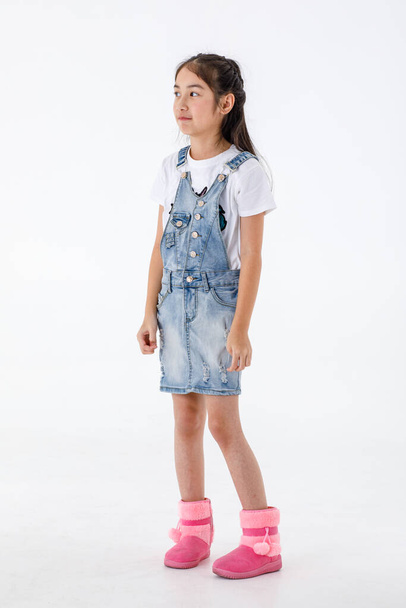 Portrait isolated studio shot of young long hair pretty cute girl in t shirt and denim skirt overalls with pink boots standing and  posing with cheerful action in front of white background. - Photo, Image