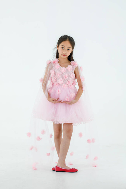 孤立したフルボディスタジオショットの少しかわいいですアジアのバレリーナ子供を身に着けていますピンクの美しいバラの花バレエドレスと赤の靴笑顔ポージングダンス幸せに白い背景の前で. - 写真・画像