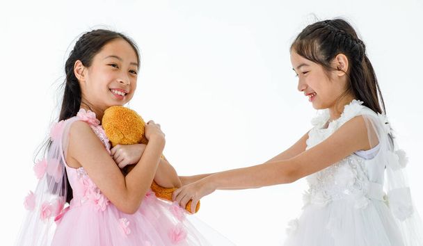 Portre, iki küçük Asyalı balerin, pembe ve beyaz güller içinde bale elbisesi giyip turuncu oyuncak ayı bebeği için gülerken çekilmiş.. - Fotoğraf, Görsel