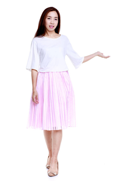 Full body of smiling young Asian female in white blouse and pink skirt pointing with hand aside isolated on white background. - Photo, Image
