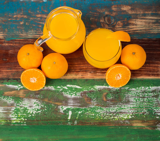 Čerstvý pomerančový džus v čiré sklenici a skleněná dekorace s čerstvým pomerančem na barevném dřevěném stole. Studio obrázek koncept pro zdravou stravu. Studio obrázek. - Fotografie, Obrázek