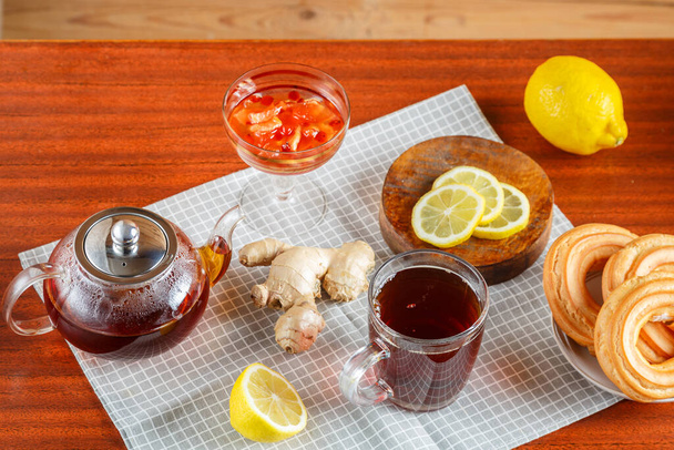 A teapot of strong tea and a cup on the table next to ginger lemon, donuts with cream. - Φωτογραφία, εικόνα