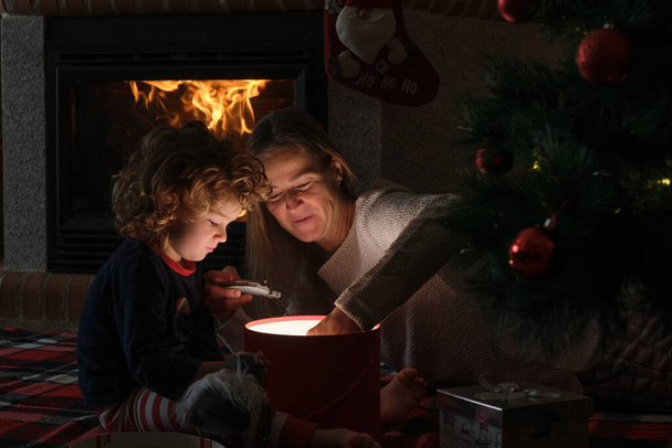 Anya és a kisfia kinyitnak egy varázslatos karácsonyi ajándékot egy karácsonyfánál. - Fotó, kép