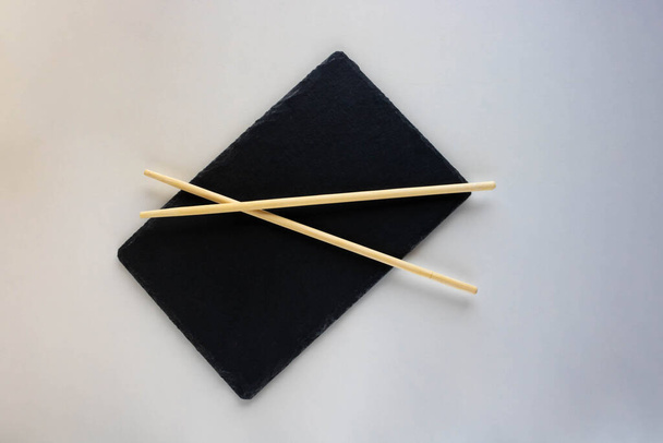Asian cuisine is a Black Slate plate with chopsticks. An empty sushi plate on a white table. - Photo, Image