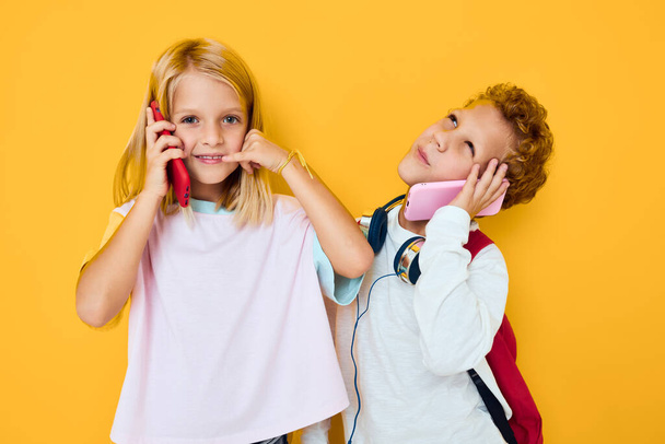 Δύο παιδιά αγόρι και κορίτσι με σχολικές τσάντες τηλεφωνική ψυχαγωγία - Φωτογραφία, εικόνα