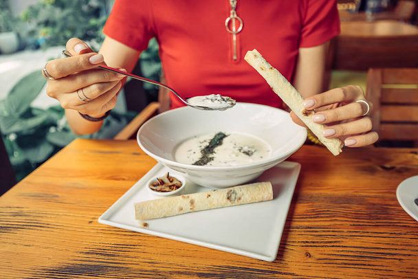 Mulher comendo prato tradicional armênio - sopa de spas feita de iogurte fermentado ou matzoon. Dois rolos de lavash em uma chapa - Foto, Imagem
