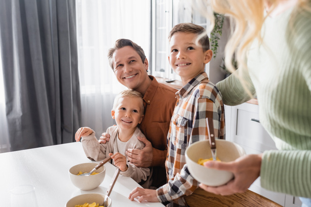 onnellinen perhe rusetteja maissi hiutaleet ottaa aamiaisen keittiössä - Valokuva, kuva