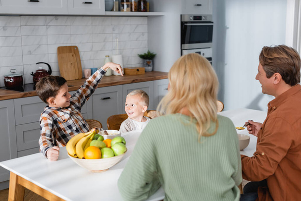 boy pointing at brother during breakfast with parents near bowl of fresh fruits - Photo, Image