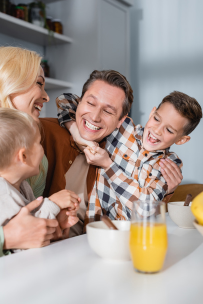 joyful family having fun during breakfast near bowls and orange juice on kitchen table - Foto, afbeelding