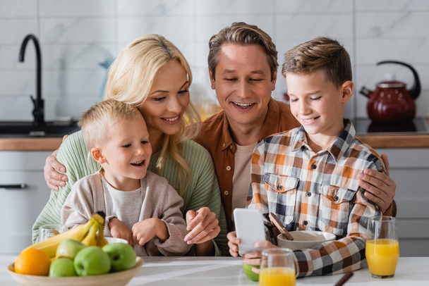 smiling boy showing smartphone to happy family during breakfast - Fotoğraf, Görsel