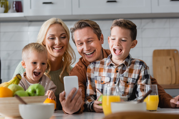 веселий чоловік бере селфі на мобільний телефон з дружиною і синами під час сніданку на кухні
 - Фото, зображення