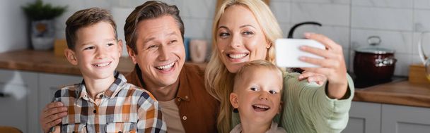 mujer alegre tomando selfie en smartphone con el marido y los hijos en la cocina, pancarta - Foto, Imagen