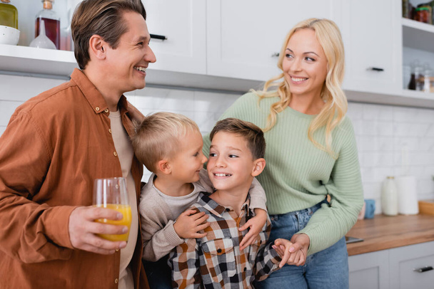marido y mujer felices mirándose cerca de hijos alegres abrazándose en la cocina - Foto, imagen