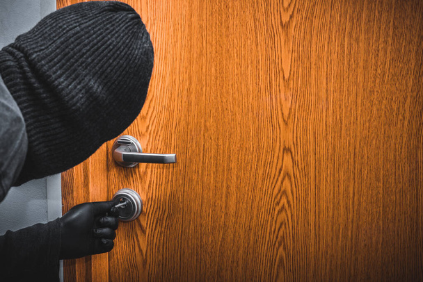 Een man in een zwarte bivakmuts en handschoenen breekt 's nachts in het appartement met een lockpick, Home verzekeringsconcept en de groeiende dreiging tijdens vakanties, Lege ruimte voor tekst  - Foto, afbeelding