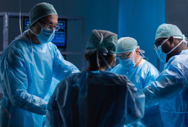 Multiracial team of professional medical surgeons performs the surgical operation in a modern hospital. Doctors are working to save the patient. Medicine, health, cardiology and transplantation. - Fotografie, Obrázek