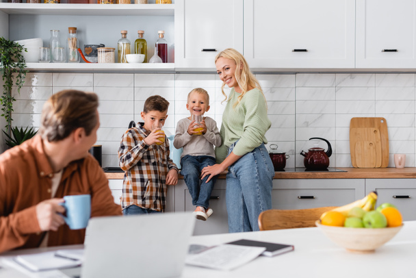 kids drinking orange juice near happy mom and father freelancer working on blurred foreground - Фото, изображение