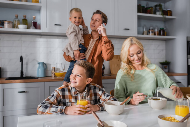 man holding kid and pouring milk in corn flakes during breakfast in kitchen - Foto, immagini