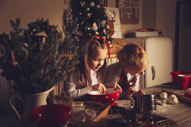 Children in the kitchen are preparing cookies. Christmas decorations, family traditions, Christmas food, holiday eve.  - Valokuva, kuva