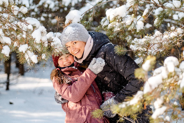 Family winter walk in the forest. Raising a child, family habits. Mother and daughter are having fun in winter in the forest in sunny frosty weather. A mother's hug. - Photo, Image
