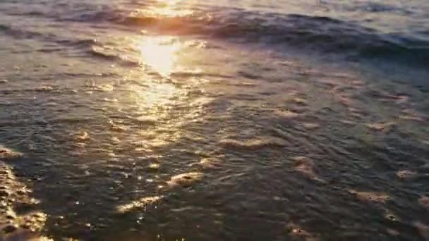 Spokojne fale morskie pluskające piaskiem plażowym w słoneczny poranek. Złoty wschód słońca odzwierciedlający - Materiał filmowy, wideo