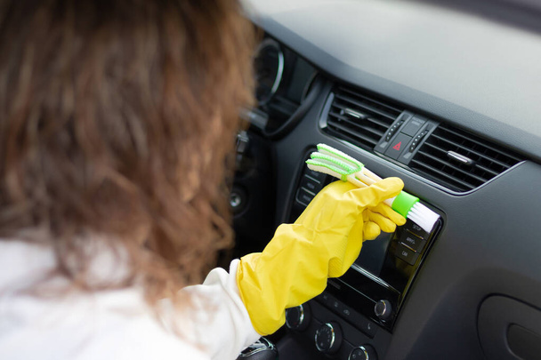 Dziewczyna w żółtych gumowych rękawiczkach wyciera deskę rozdzielczą samochodu z kurzu specjalną szczotką w jasny jesienny dzień. Wybiórcze skupienie. Zbliżenie - Zdjęcie, obraz