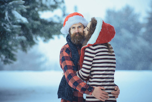 Christmas couple of happy man and woman. Couple in love with red santa claus hat in winter outdoor. Winter holiday and vacation - Foto, imagen
