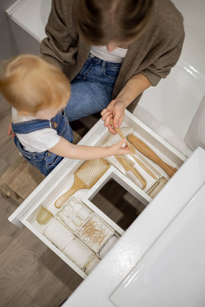 Mom and little daughter organizing bathroom storage, displaying beauty cosmetic creams and toiletries in drawer - Fotografie, Obrázek