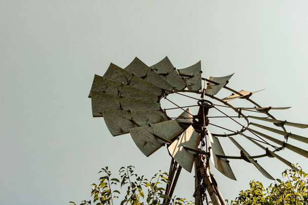 Vintage windmill against backdrop of grey sky and surrounded by green plants at base. Ontario, Canada. - Photo, Image