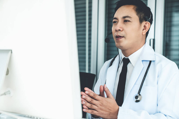 Medico indossando auricolare parlando attivamente in videochiamata in una clinica o in ospedale . - Foto, immagini