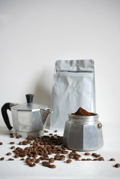        Turk com café moído e grãos de café em uma mesa branca e um fundo leve.                         - Foto, Imagem