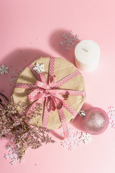 Christmas or New Year gift concept in pink tones. Wrapper box, tied bow, dry flowers, and festive toy. Zero Waste style, trendy hard light, dark shadow, rosy background, top view - Foto, imagen