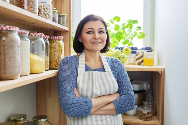 Portrait of a smiling woman in an apron in the kitchen in the pantry. - Fotó, kép
