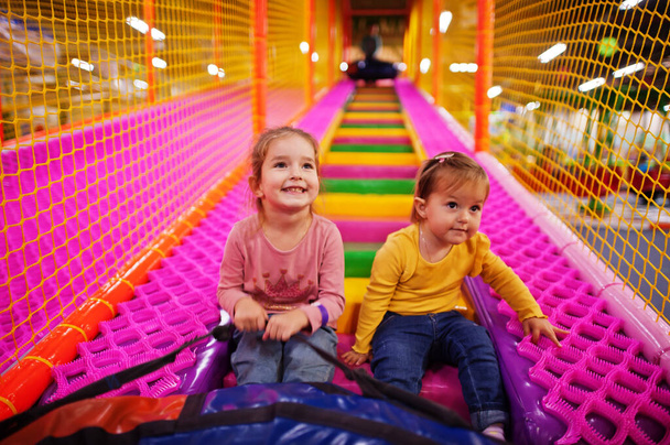 Two sisters sitting in tubing donuts enjoying slides in fun children center. - Фото, изображение